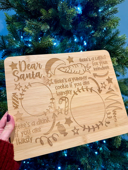 Wooden Christmas platter with engraved text in front of a decorated Christmas tree.