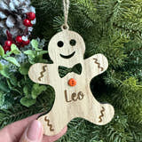 Load image into Gallery viewer, Wooden gingerbread man ornament with a face held in front of a Christmas tree.