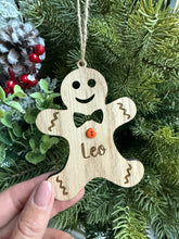 Load image into Gallery viewer, Wooden gingerbread man ornament with a face held in front of a Christmas tree.