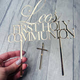 Load image into Gallery viewer, Gold 'Leo's First Holy Communion' cake topper with a cross on a wooden surface.