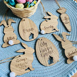 Load image into Gallery viewer, A set of seven wooden hanging Easter decorations, including bunny shapes and an egg design, with personalized engravings of names.