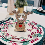 Load image into Gallery viewer, Wooden reindeer place name holder with red nose and engraved name “Mum” on a festive Christmas dinner table with holly plates and holiday decorations.