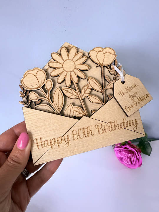 Wooden birthday card with floral design and 'Happy 80th Birthday' text, held by a hand.