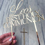 Load image into Gallery viewer, Gold 'Leo's First Holy Communion' cake topper with a cross on a wooden surface.