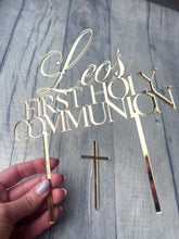 Load image into Gallery viewer, Gold 'Leo's First Holy Communion' cake topper with a cross on a wooden surface.