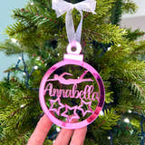 Load image into Gallery viewer, A hand holding a pink Christmas tree decoration with the text 'Anna' and star graphics, with a bow on top.