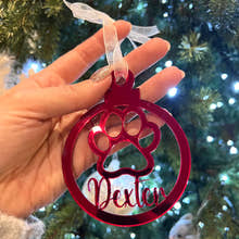 Load image into Gallery viewer, A hand holding a red Christmas tree decoration with a paw print design and the name 'Dexter' written on it.