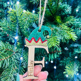 Load image into Gallery viewer, A hand holding a Christmas tree decoration featuring a laser cut and engraved oak veneer elf with a crown and the initial 'F' on it, with blurred green pine needles in the background.