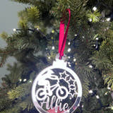 Load image into Gallery viewer, A hand holding a silver-colored Christmas tree decoration with a BMX bike and stars design, with a red hanging ribbon and lights in the background.