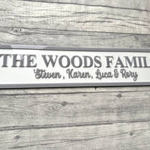 Load image into Gallery viewer, Family name plaque on a wooden surface with flowers in the corner