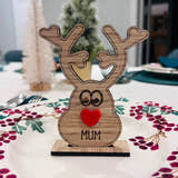Load image into Gallery viewer, Wooden reindeer place name holder with red nose and engraved name “Mum” on a festive Christmas dinner table with holly plates and holiday decorations.