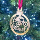 Load image into Gallery viewer, A gold-colored Christmas tree decoration featuring the text 'DANIEL' and a representation of a BMX bike, hanging from a red ribbon on a Christmas tree with green needles and decoration lights.
