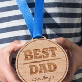 Load image into Gallery viewer, Best dad wooden medal Fathers Day gift held by Dad with blue ribbon and gift background UK