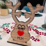 Load image into Gallery viewer, Wooden reindeer place name holder with red nose and engraved name “Mum” on a festive Christmas dinner table with holly plates and holiday decorations.