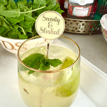 Load image into Gallery viewer, Glass of cocktail with mint leaves and a 'Seventy & Sloshed' stirrer, surrounded by bottles and ingredients on a countertop.