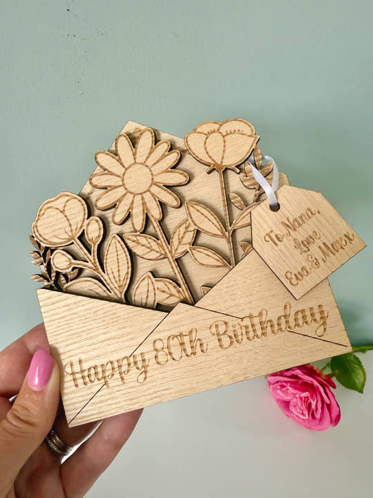 Wooden card with floral design and 'Happy 80th Birthday' text, held by a hand.