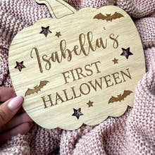 Load image into Gallery viewer, Wooden pumpkin-shaped sign with 'Isabella's First Halloween' text on a textured fabric background