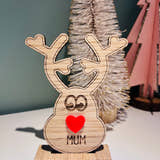 Load image into Gallery viewer, Wooden reindeer place name holder with red nose and engraved name “Mum” on a festive Christmas dinner table with holly plates and holiday decorations.