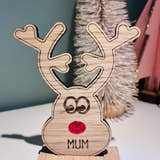 Load image into Gallery viewer, Wooden reindeer place name holder with red nose and engraved name “Mum” on a festive Christmas dinner table with holly plates and holiday decorations.