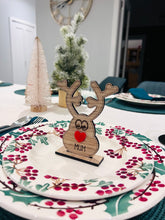 Load image into Gallery viewer, Wooden reindeer place name holder with red nose and engraved name “Mum” on a festive Christmas dinner table with holly plates and holiday decorations.