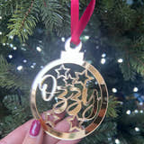 Load image into Gallery viewer, A hand holding a gold-colored Christmas tree decoration with the word 'Stars' and a star graphic, with a red ribbon hanging from the top.