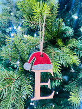 Load image into Gallery viewer, A decorative Christmas tree ornament in the shape of a Santa hat with the letter 'E' on it, hanging on a tree with lights and pine needles in the background.