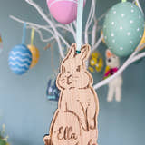 Load image into Gallery viewer, A wooden hanging bunny decoration with the name 'Ella' inscribed, displayed among colorful Easter eggs on a tree.