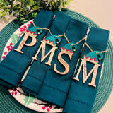 Load image into Gallery viewer, Personalized oak veneer name place settings on a green fabric, with 'PMS' and 'Santa' options, decorated with twine and sparkle, displayed on a plate with a Christmas tree in the background.