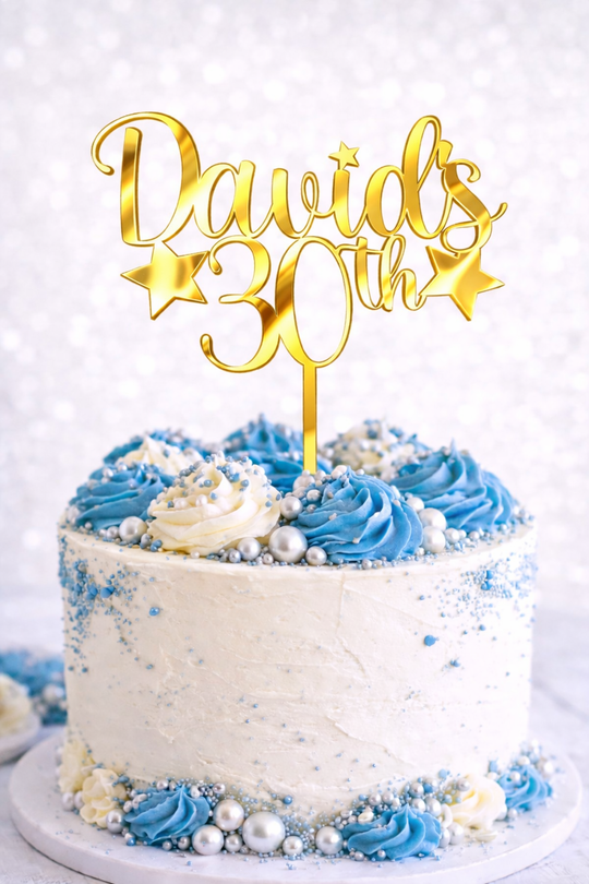Personalised gold mirror acrylic birthday cake topper with custom name and age on white celebration cake with blue buttercream and silver decorations.