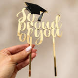 Load image into Gallery viewer, Gold mirrored acrylic graduation cake topper with black graduation cap, handmade in the UK, displayed by hand against a neutral background.