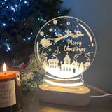 Load image into Gallery viewer, A clear acrylic snowglobe with a 'Merry Christmas' message, illuminated from within, placed on a table with a blurred Christmas tree and gifts in the background.