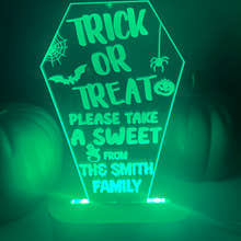 Load image into Gallery viewer, An LED light up stand with a personalized Halloween message 'Trick or Treat, Please Take a Sweet from The Smith Family' displayed on it. The stand is green and has a pumpkin-like shape with decorative elements and text.