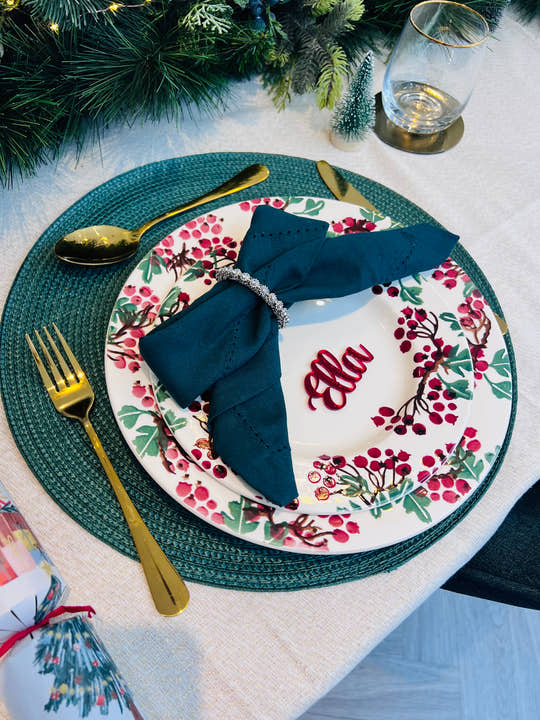 Christmas dinner table setting with personalised acrylic place name ‘Ella’ in red, festive plate and green napkin