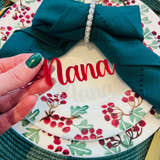 Load image into Gallery viewer, Hand holding personalised red acrylic place name ‘Nana’ on Christmas dinner plate with holly berry design
