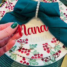 Load image into Gallery viewer, Hand holding personalised red acrylic place name ‘Nana’ on Christmas dinner plate with holly berry design