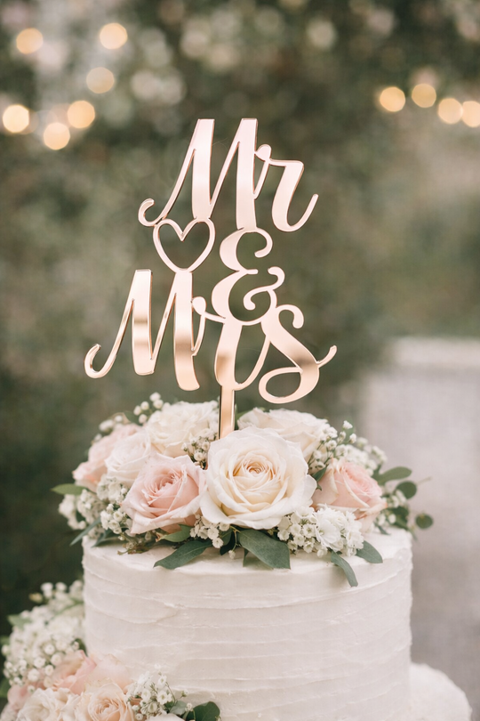 Rose Gold mirror acrylic Mr and Mrs wedding cake topper on a white buttercream wedding cake with blush roses and greenery.