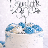 Load image into Gallery viewer, Personalised silver mirror acrylic birthday cake topper with custom name and age on white celebration cake with blue buttercream and silver decorations.