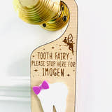 Load image into Gallery viewer, Personalised wooden Tooth Fairy door hanger with engraved text and white tooth shape with purple bow, hanging on a brass doorknob