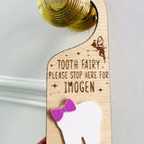 Load image into Gallery viewer, Personalised wooden Tooth Fairy door hanger with engraved text and white tooth shape with purple bow, hanging on a brass doorknob