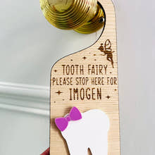 Load image into Gallery viewer, Personalised wooden Tooth Fairy door hanger with engraved text and white tooth shape with purple bow, hanging on a brass doorknob