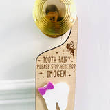 Load image into Gallery viewer, Personalised wooden Tooth Fairy door hanger with engraved text and white tooth shape with purple bow, hanging on a brass doorknob