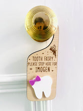 Load image into Gallery viewer, Personalised wooden Tooth Fairy door hanger with engraved text and white tooth shape with purple bow, hanging on a brass doorknob