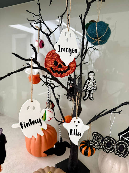 Personalised ghost Halloween tree decoration with engraved name hanging on a Halloween tree with pumpkins and spooky ornaments.
