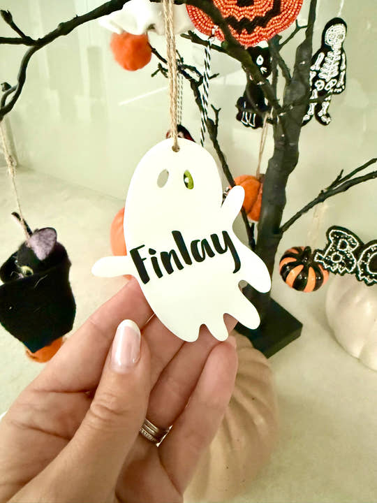 Personalised ghost Halloween tree decoration with engraved name hanging on a Halloween tree with pumpkins and spooky ornaments.
