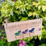 Load image into Gallery viewer, Personalised wooden sign reading “Grandad’s Greenhouse – Little Helpers Welcome” with a plant pot labelled with childrens names, hanging inside a bright sunny garden.