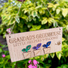 Load image into Gallery viewer, Personalised wooden sign reading โGrandadโs Greenhouse โ Little Helpers Welcomeโ with a plant pot labelled with childrens names, hanging inside a bright sunny garden.