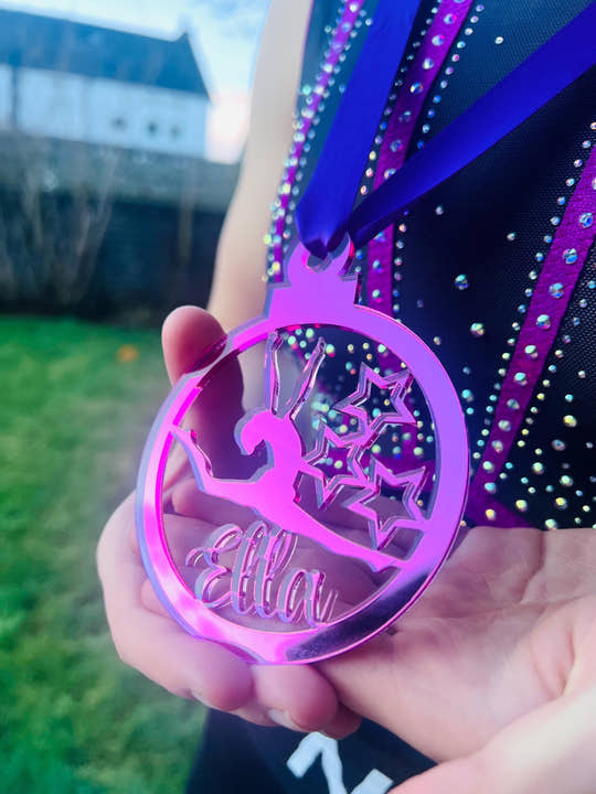 Hand holding a purple personalised gymnast medal, showing its size