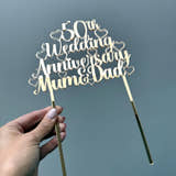 Load image into Gallery viewer, Personalised gold mirror acrylic 50th Wedding Anniversary Mum & Dad cake topper held in a hand, showing its size