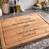 Load image into Gallery viewer, Personalised bamboo cheeseboard engraved with “Sweet dreams are made of Cheese” and custom names, displayed on a granite kitchen worktop.