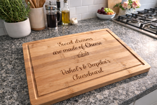 Personalised bamboo cheeseboard engraved with “Sweet dreams are made of Cheese” and custom names, displayed on a granite kitchen worktop.